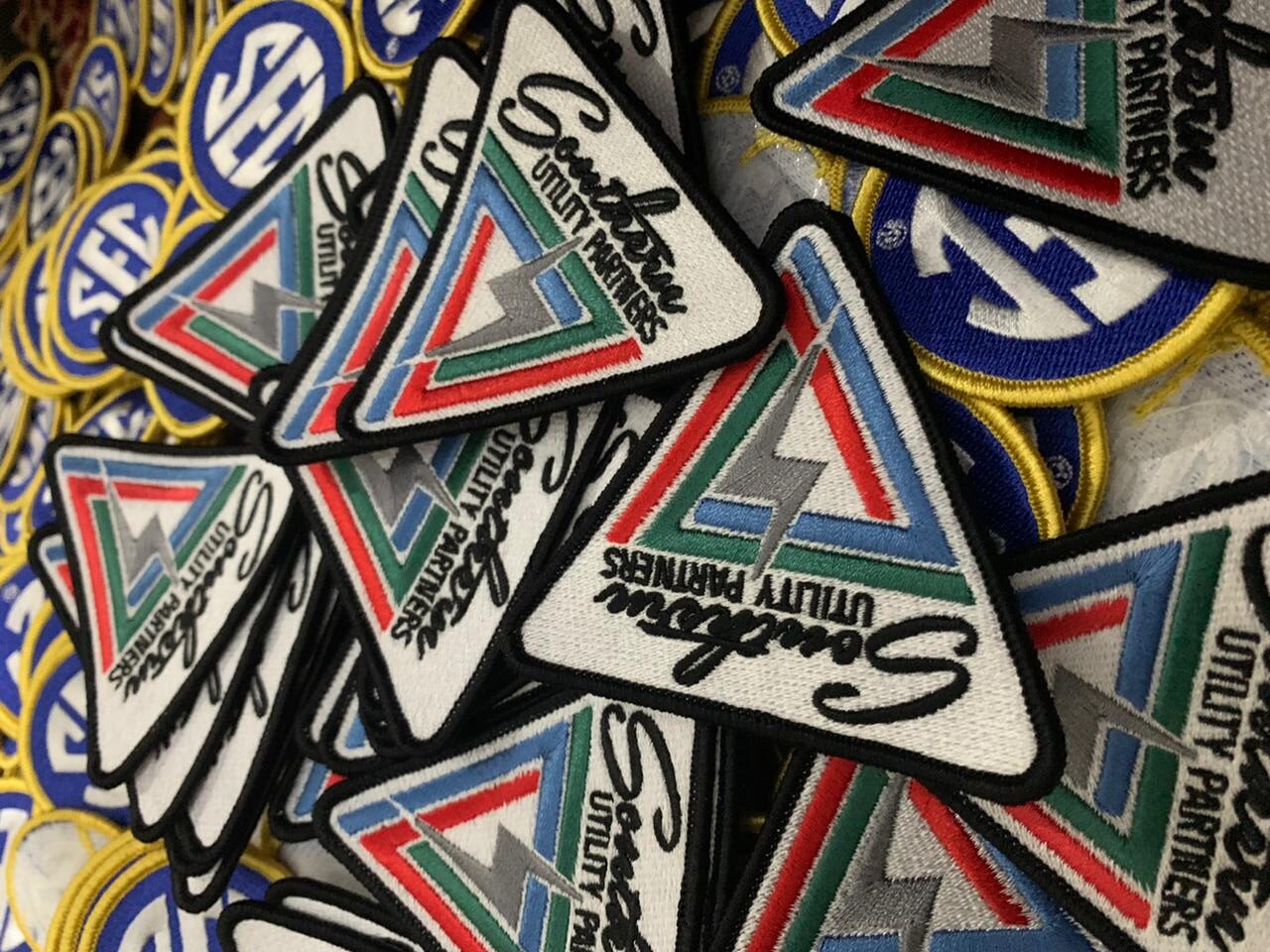 The image displays a collection of colorful, custom-designed patches. Each patch features unique graphics and text, representing various organizations or themes.