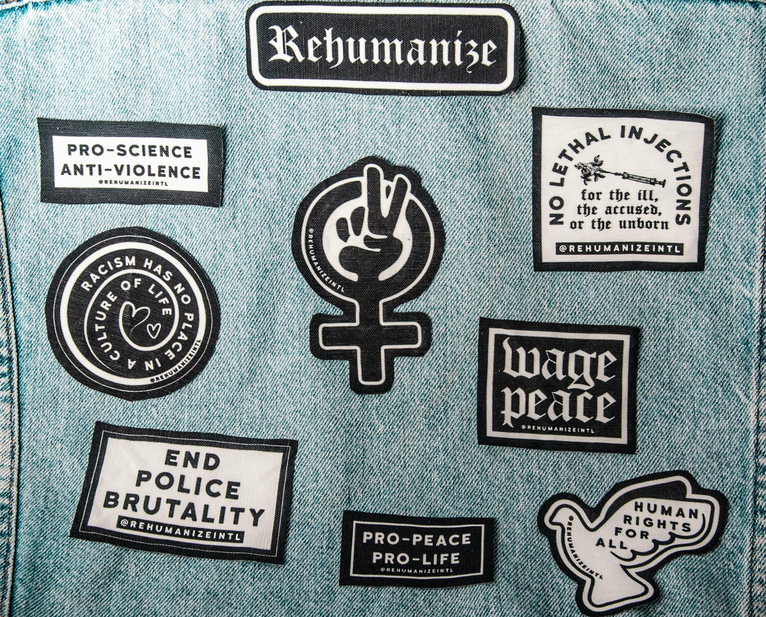 A close-up image of denim fabric featuring multiple black-and-white patches with social justice messages